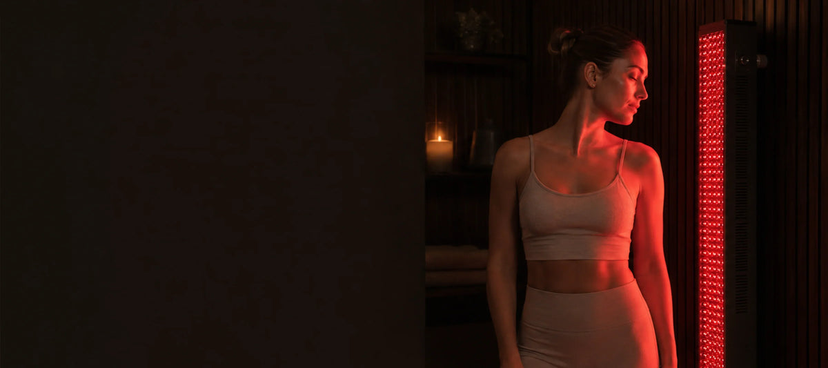 Woman relaxing under red light therapy panel for home recovery and wellness